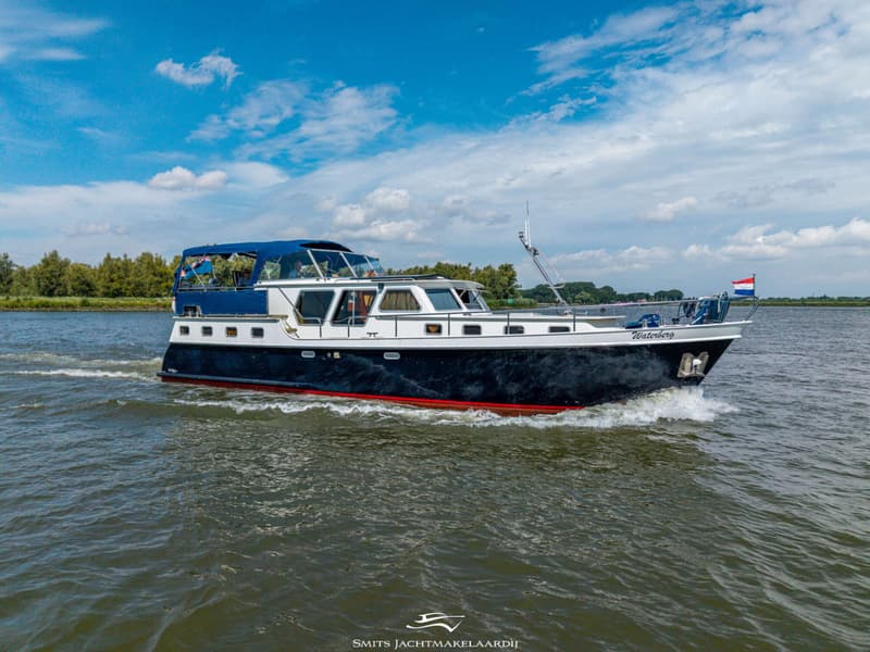 Een donkerblauwe motorboot met witte opbouw en een blauwe bimini vaart over het water onder een blauwe lucht.