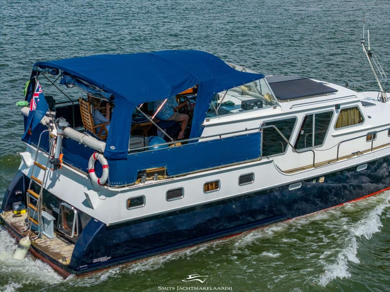 Een blauw-witte motorboot met een blauwe kap vaart op het water, met twee personen aan boord.