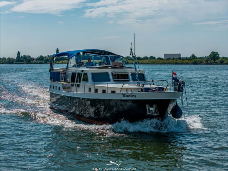 Een donkerblauwe motorboot met witte opbouw en blauwe bimini vaart op een zonnige dag over het water.