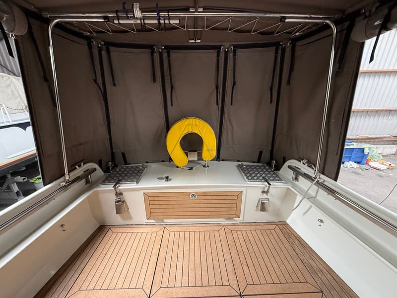 De foto toont de achterkant van een boot met een bruine cabrioletkap, een gele reddingsboei en een houten vloer.