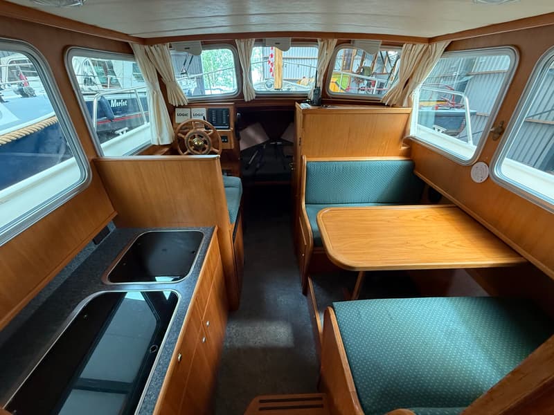 De foto toont het interieur van een boot met een stuurwiel, een keukenblok, een tafel en zitbanken. — Barkas Barkas 8.30 OK