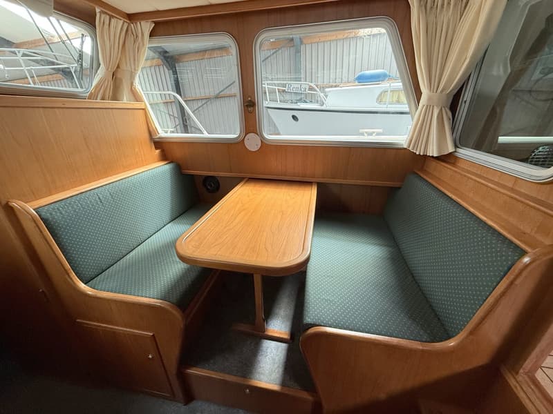De foto toont het interieur van een boot met houten wanden, twee groene banken en een houten tafel. — Barkas Barkas 8.30 OK