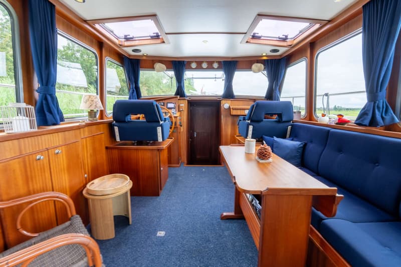 De foto toont het interieur van een boot met houten lambrisering, blauwe bekleding en een stuurstand.