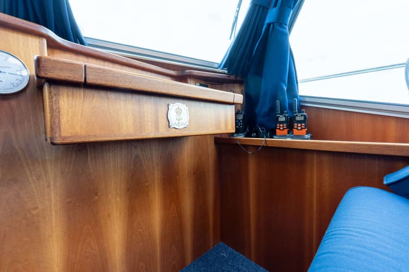 Een interieur van een boot met houten wanden, een blauw gordijn en drie portofoons op een plank.