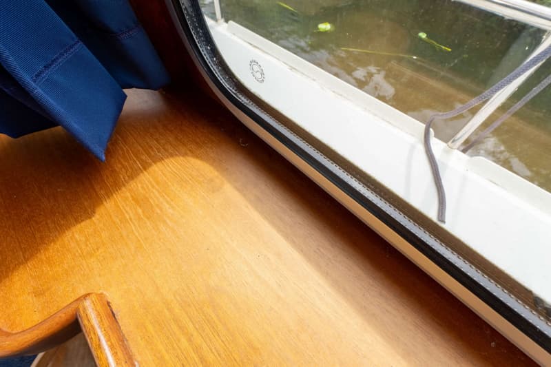 Een houten oppervlak met een blauw gordijn en een raam waardoor water met planten zichtbaar is.