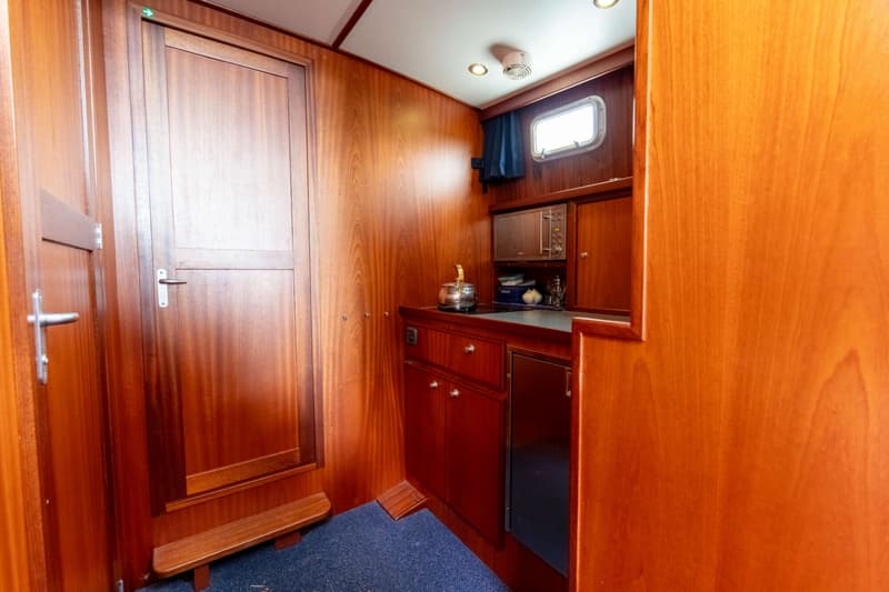 Een houten kajuit met een kombuis, een deur, een raam en een blauw tapijt op de vloer. — Brandsma Brandsma 11.00 OK SP