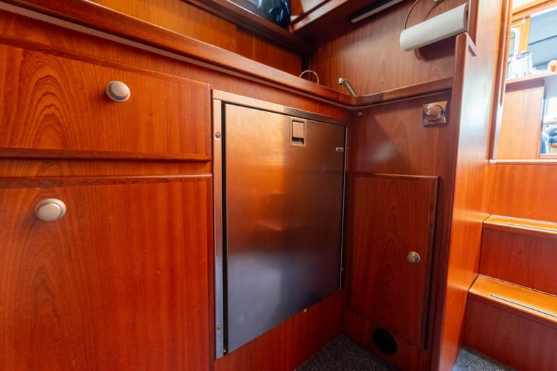 Een roestvrijstalen koelkast is ingebouwd in een houten interieur met kasten, een kraan en een papieren handdoekhouder.