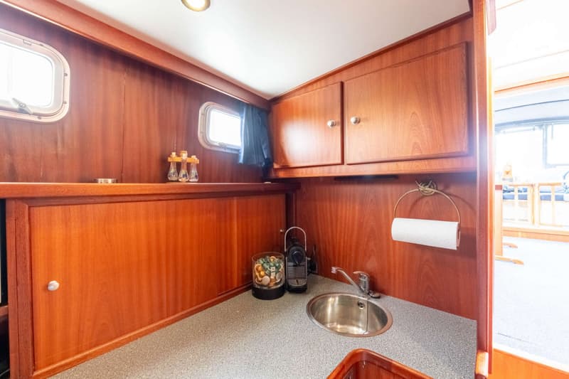 Een houten kombuis met een aanrecht, spoelbak, kraan, koffiezetapparaat, capsulehouder en papieren handdoekhouder.