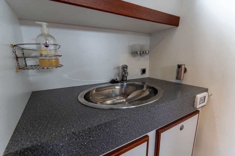 Een rvs-spoelbak met kraan is ingebouwd in een donkergrijs aanrechtblad, met daarboven een houten plank en een zeepdispenser.