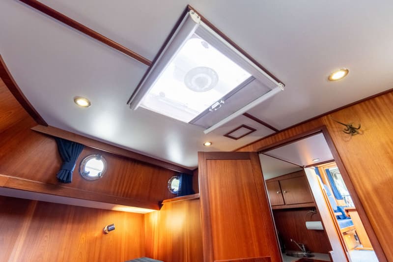 Een interieur van een boot met houten wanden, een wit plafond met inbouwspots en een open dakluik.