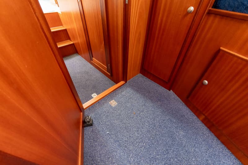 Een interieur van een boot met houten wanden en een blauwe vloerbedekking, met een trapje zichtbaar.
