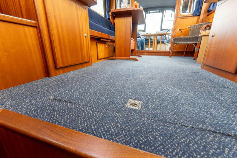De foto toont het interieur van een boot met een blauw tapijt op de vloer en houten wanden en meubilair.
