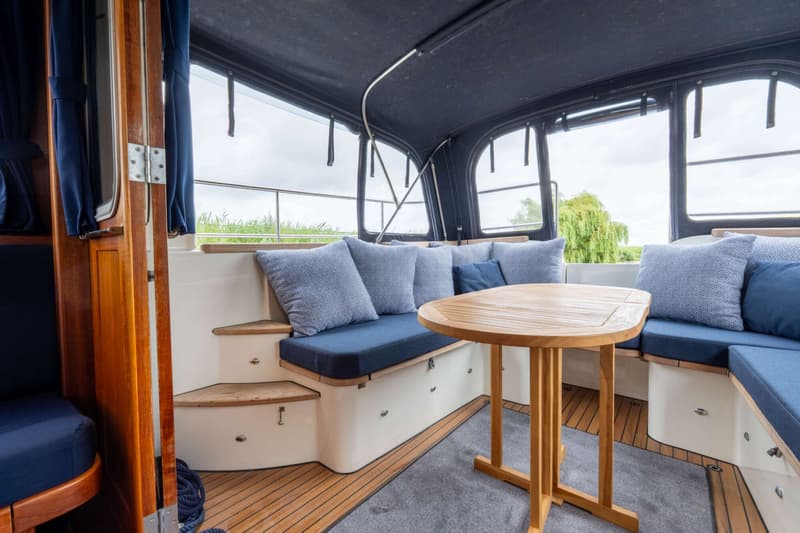 Een interieur van een boot met een houten tafel, blauwe kussens en een donkerblauw dak. — Brandsma Brandsma 11.00 OK SP