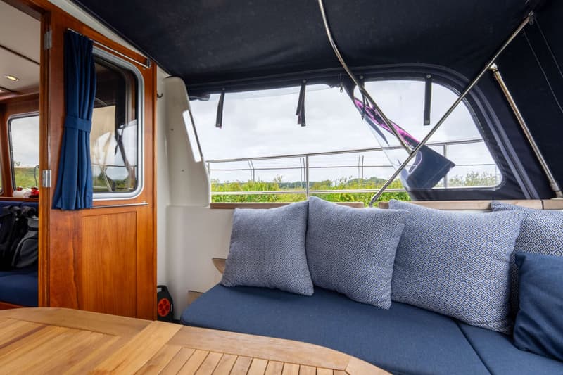Een houten tafel en bank met kussens zijn zichtbaar onder een donkerblauwe kap met doorzichtige ramen.