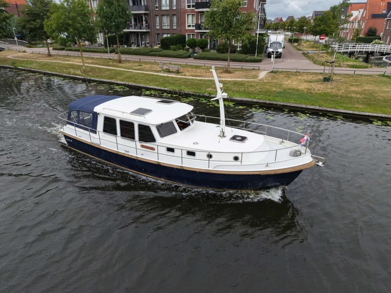 Een blauw-witte boot met een blauwe kap vaart op een kanaal langs een woonwijk. — Brandsma Brandsma 11.00 OK SP
