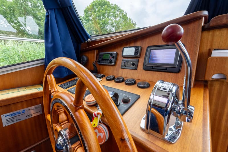 Een houten stuurwiel en dashboard met diverse meters, een Garmin-scherm en een chromen gashendel zijn zichtbaar.
