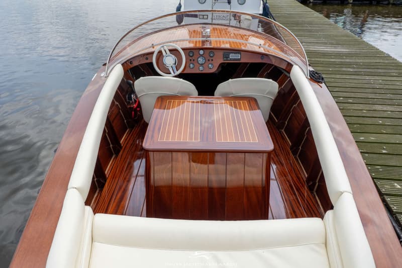 Een houten boot met een glanzende afwerking en lichte bekleding ligt aan een houten steiger. — Divank Divank Uscire 635