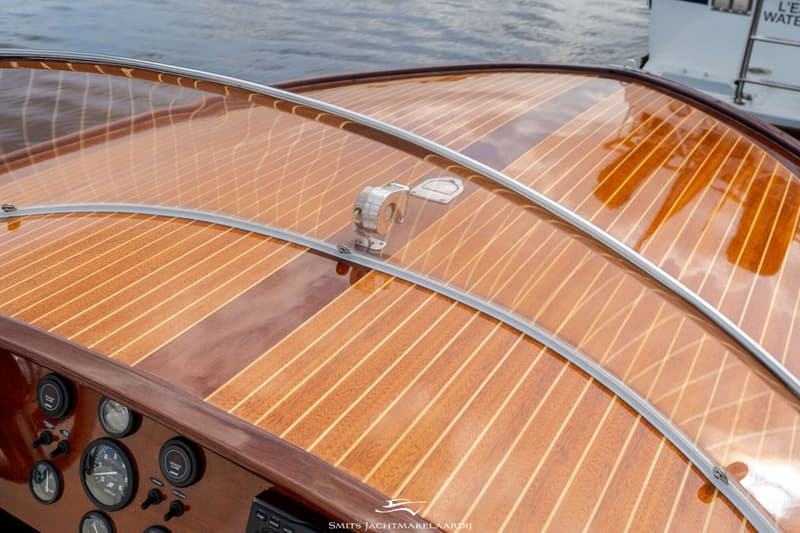 Een detailfoto van een houten bootdek met een transparante windscherm en een deel van het dashboard.
