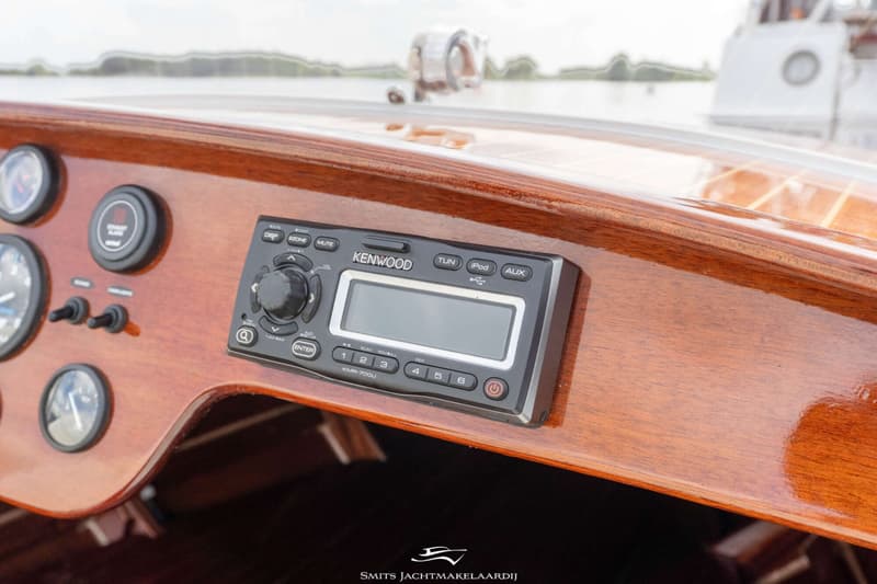 Een Kenwood KMR-700U radio is ingebouwd in een glanzend houten dashboard met diverse meters en schakelaars.