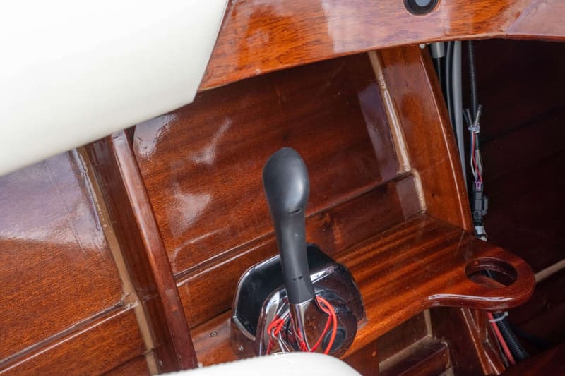 Een close-up van een zwarte gashendel met chromen basis, gemonteerd op een glanzend gelakte houten zijwand.