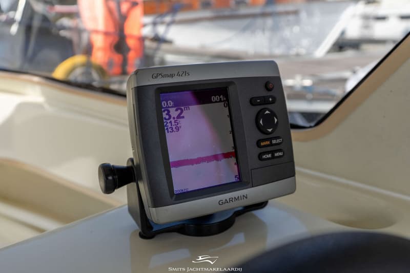 Een Garmin GPSmap 421s plotter/dieptemeter staat op een wit oppervlak met een oranje reddingsvest op de achtergrond.