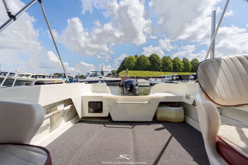 De foto toont de achterkant van een boot met een buitenboordmotor, een grijze vloerbedekking en twee stoelen.