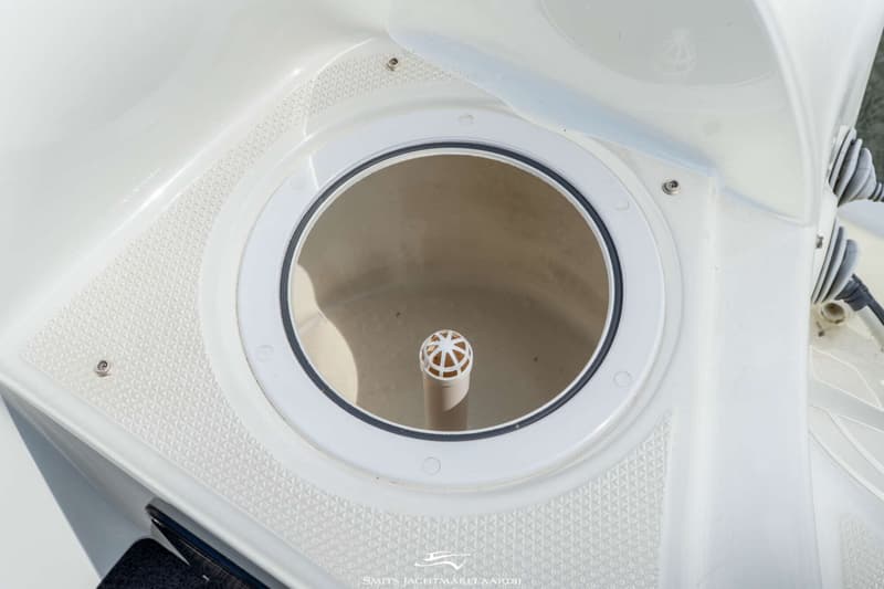 Een open rond luik met een zwarte rubberen rand en een witte buis met een geperforeerde bol in het midden.