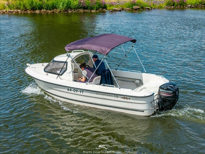 Een witte boot met twee personen aan boord vaart op het water, met een paarse biminitop en een Mercury buitenboordmotor.
