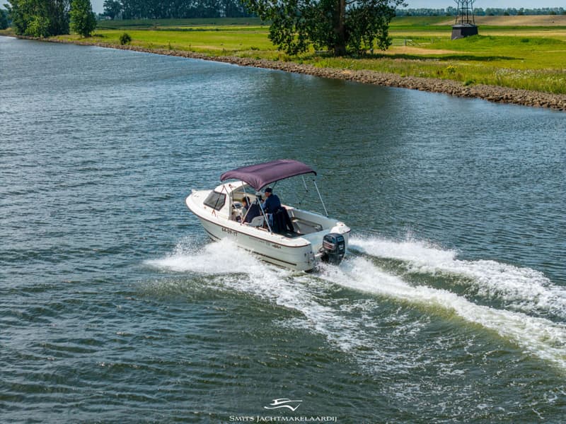 Een witte motorboot met een paarse biminitop vaart over het water, met twee personen aan boord.