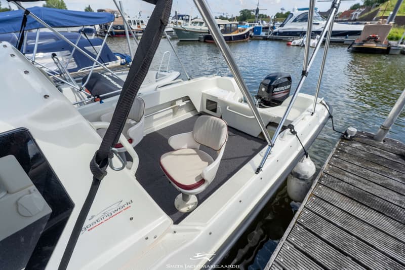 Een witte boot met een zwarte Mercury buitenboordmotor ligt afgemeerd aan een houten steiger.