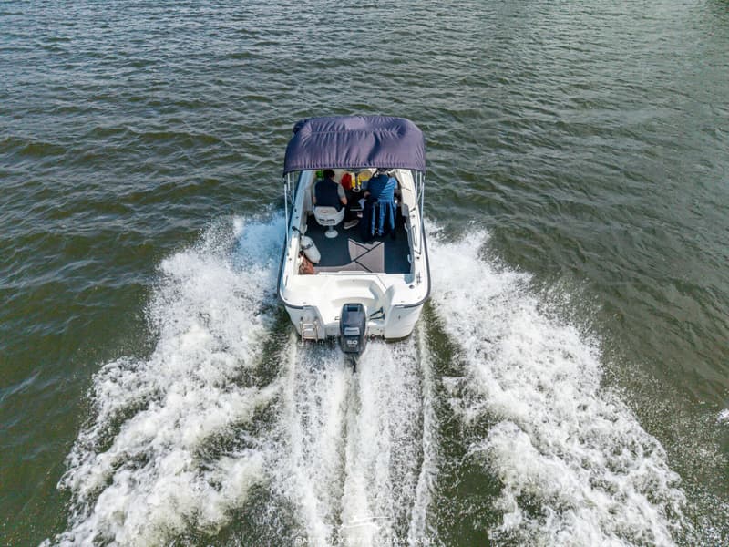 Een witte motorboot met twee personen aan boord vaart over water, met een spoor van schuim achter zich.