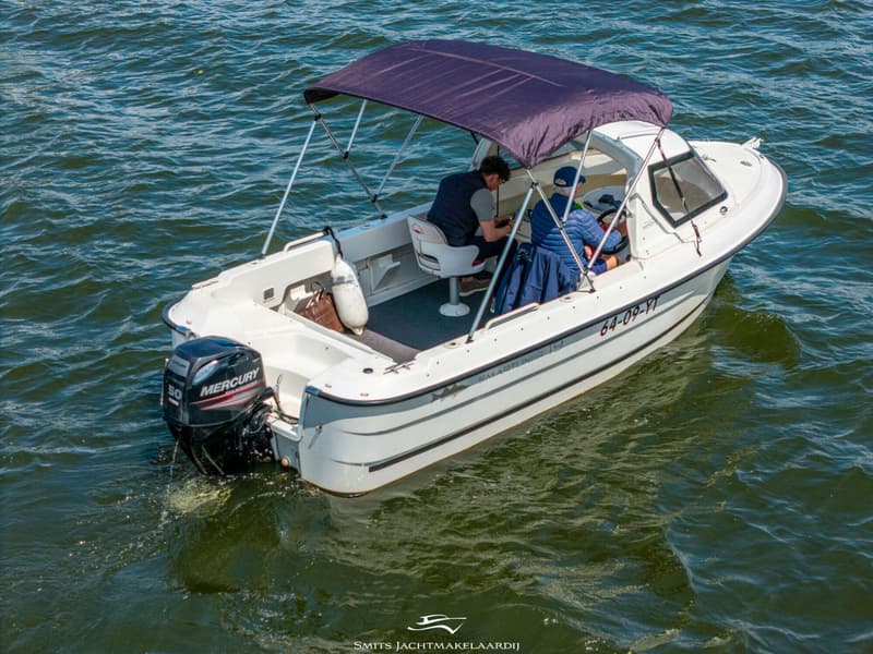 Een witte motorboot met twee opvarenden en een donkerblauwe biminitop vaart op groen water. — Smartliner Smartliner 19 Cuddy