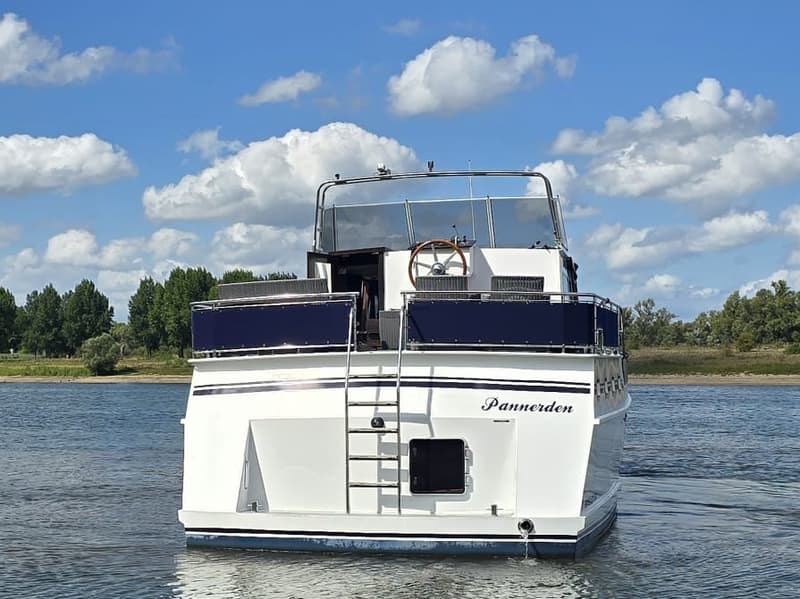 Een witte motorboot met de naam "Pannerden" op de spiegel, een zwemtrap en een stuurwiel op het bovendek.