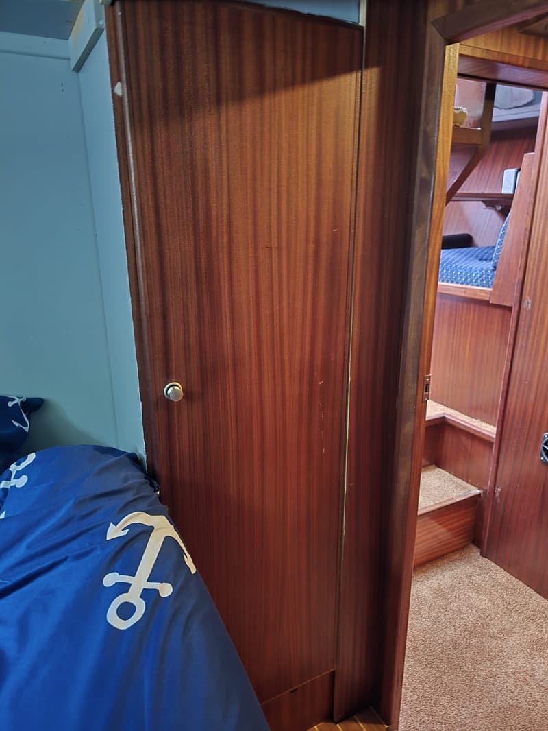 Een interieur van een boot met een houten deur, een blauw dekbed met ankerpatroon en een trap met tapijt.