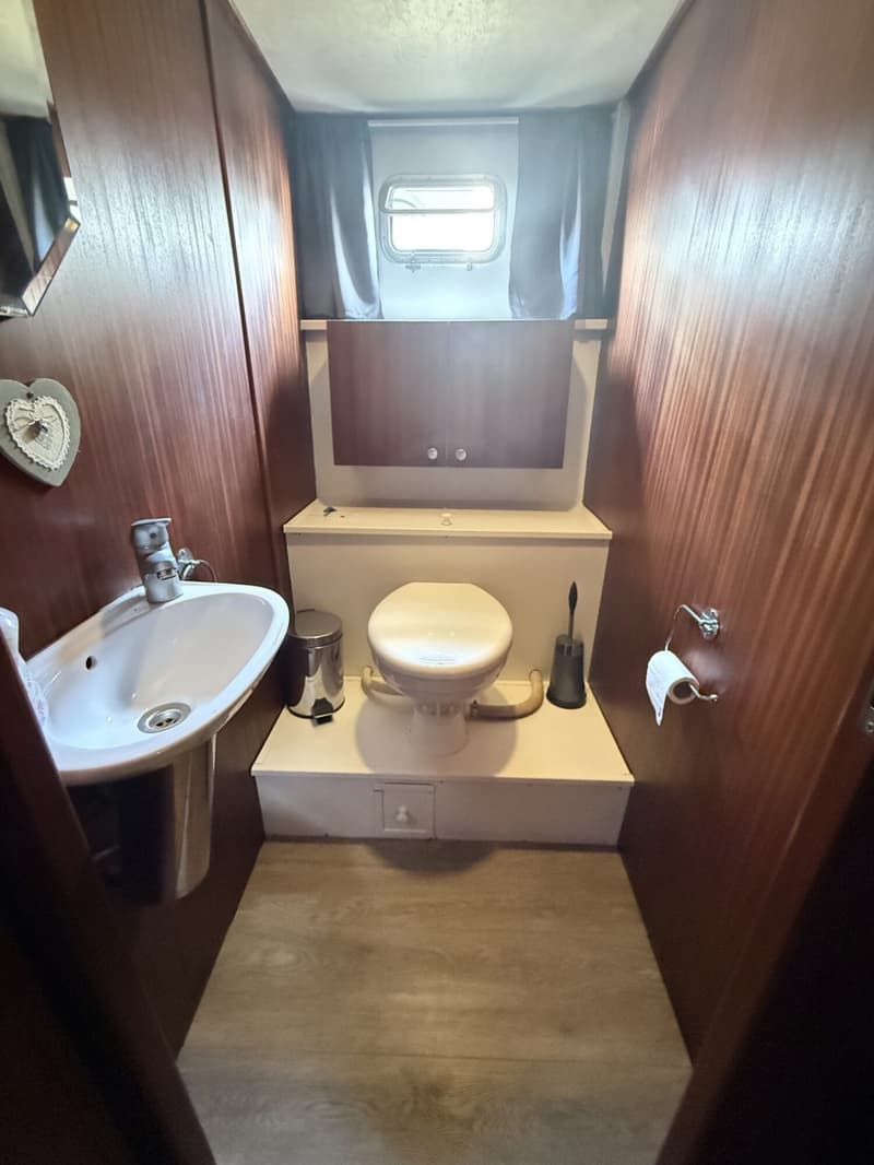 Een kleine badkamer met een wastafel, toilet, spiegel, toiletrolhouder en een raam met gordijnen.