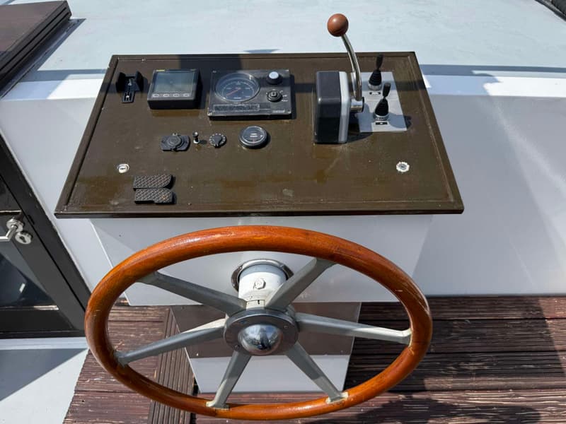Een houten stuurwiel en een bedieningspaneel met diverse meters en hendels zijn zichtbaar op een boot.