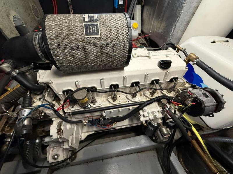 Een close-up van een scheepsmotor met een groot luchtfilter en diverse leidingen en kabels.