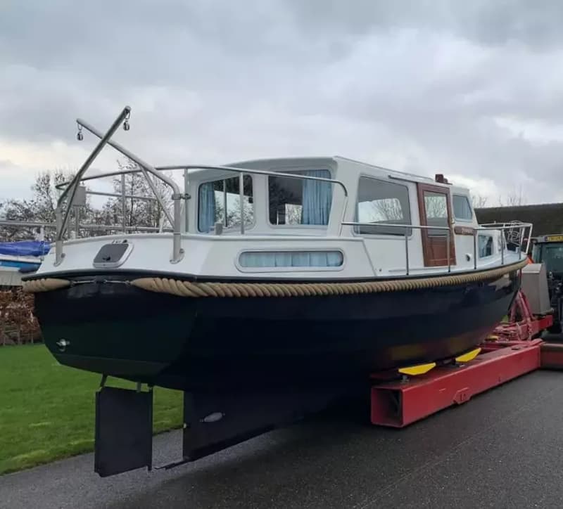 Een blauw-witte motorboot staat op een rode trailer op een geasfalteerde ondergrond onder een bewolkte hemel.