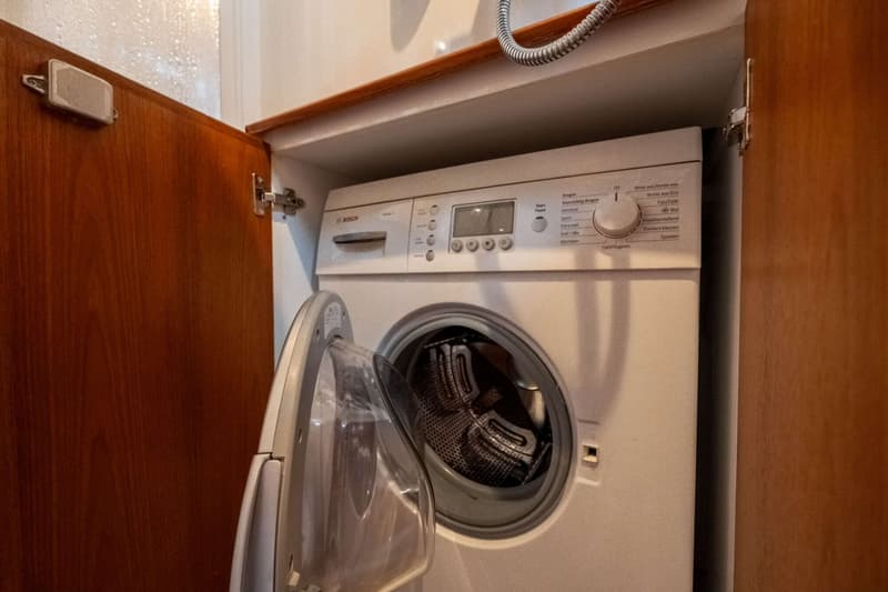 Een witte Bosch wasmachine met een open deur is zichtbaar, ingebouwd in een houten kast.