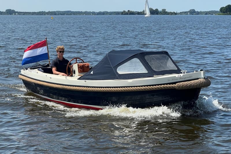 Een man met zonnebril bestuurt een donkerblauwe sloep met een Nederlandse vlag aan de achterkant op een meer. — Interboat 19