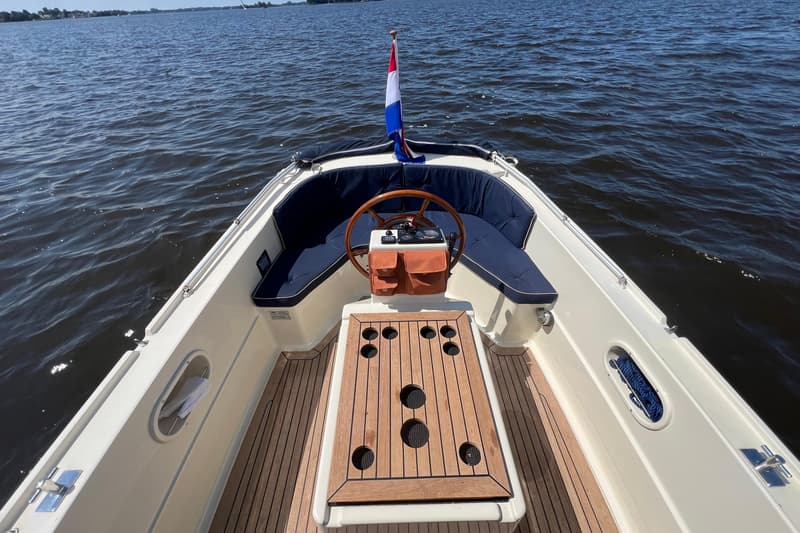 Een boot met een houten stuurwiel, een Nederlandse vlag, blauwe kussens en een houten tafel met bekerhouders. — Interboat 19