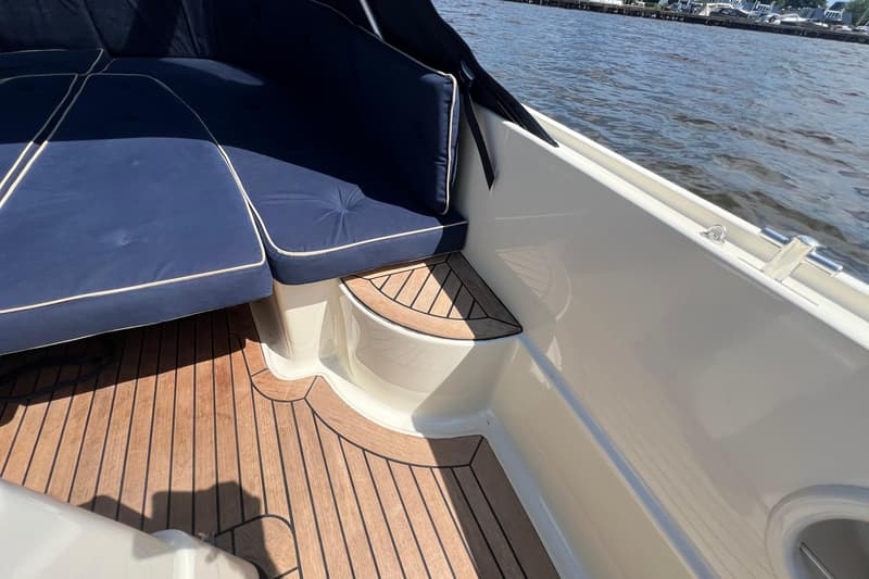 Een detailfoto van een bootinterieur met blauwe kussens, een houten vloer en een deel van het wateroppervlak.