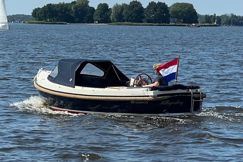 Een donkerblauwe sloep met een crèmekleurige bovenrand en een donkerblauwe kap vaart op het water. — Interboat 19