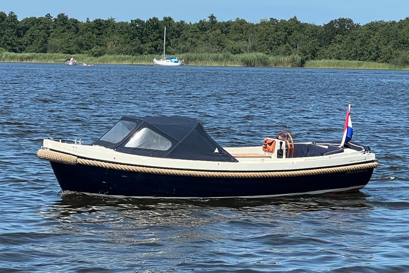 Een donkerblauwe sloep met een crèmekleurige bovenkant en een donkerblauwe kap vaart op het water. — Interboat 19