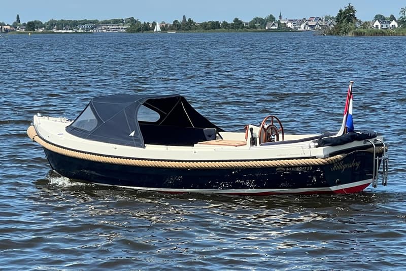 Een donkerblauwe sloep met een crèmekleurige bovenkant en een donkerblauwe buiskap vaart op het water. — Interboat 19
