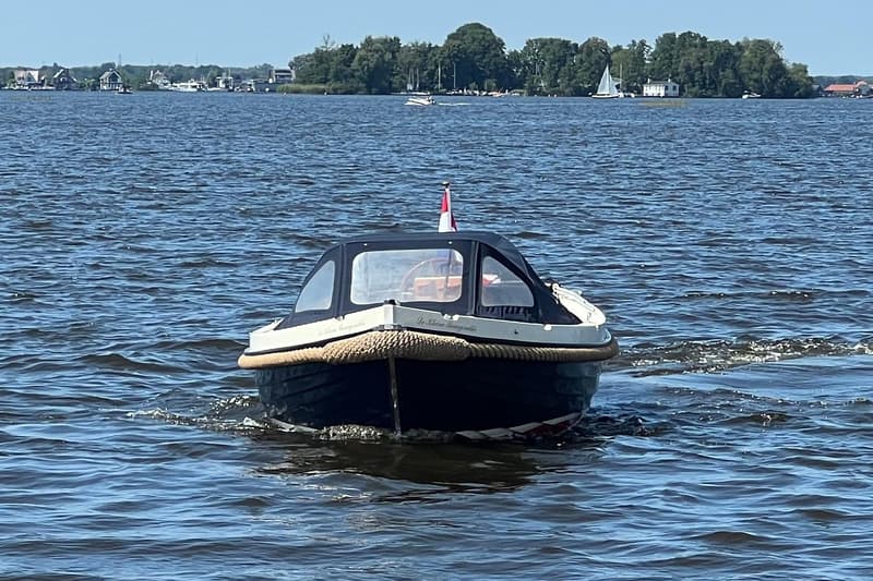 Een donkerblauwe sloep met een lichtbeige stootrand en een donkerblauw dekzeil vaart op het water. — Interboat 19