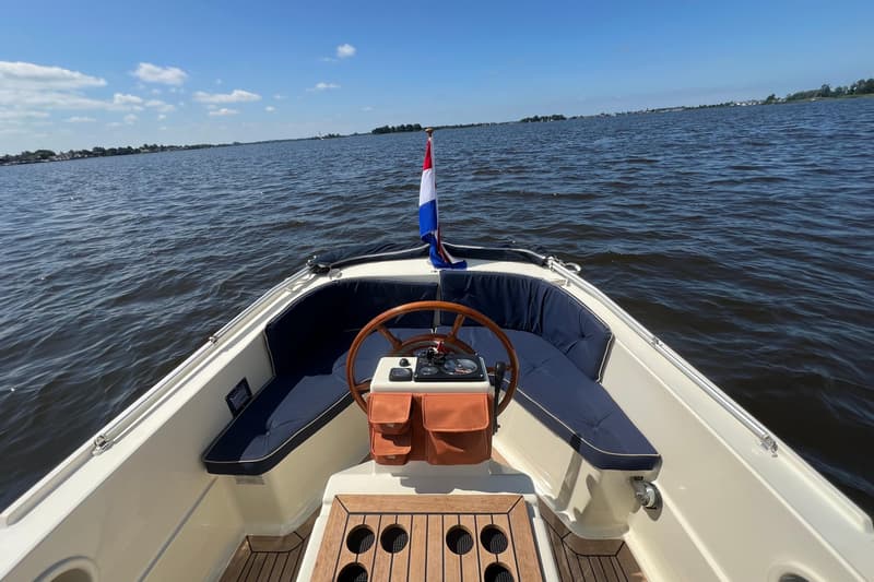 Een boot met een houten stuurwiel en blauwe kussens op het dek, met een Nederlandse vlag aan de boeg. — Interboat 19