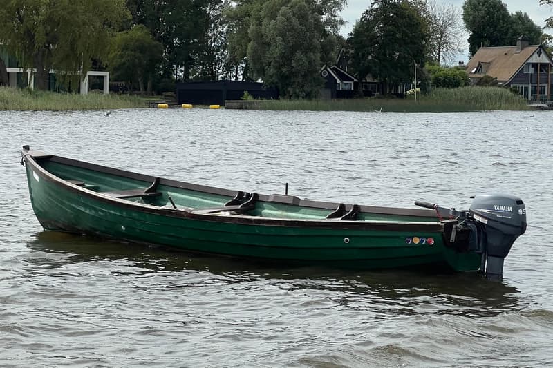 Een groene roeiboot met een Yamaha 9.9 Four Stroke buitenboordmotor ligt in het water.