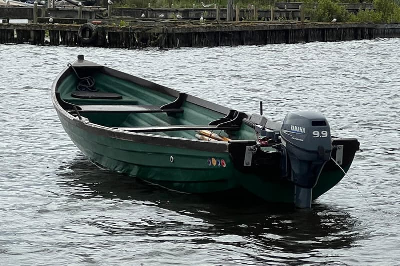 Een groene roeiboot met een Yamaha 9.9 buitenboordmotor ligt in het water, met een houten steiger op de achtergrond.