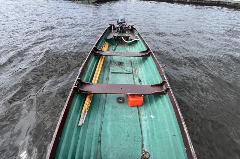 Een groene roeiboot met een buitenboordmotor en roeiriemen, drijvend op water.